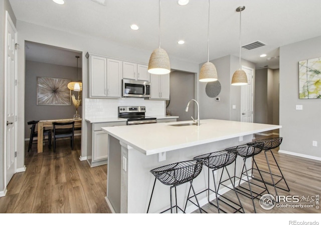 kitchen featuring sink, tasteful backsplash, pendant lighting, a kitchen island with sink, and appliances with stainless steel finishes