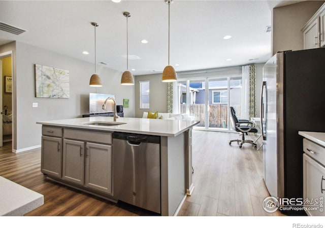 kitchen with pendant lighting, stainless steel appliances, an island with sink, wood-type flooring, and sink