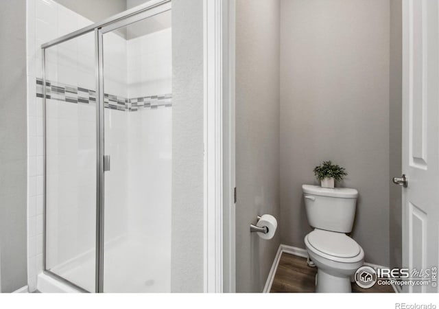 bathroom featuring toilet, a shower with door, and hardwood / wood-style floors