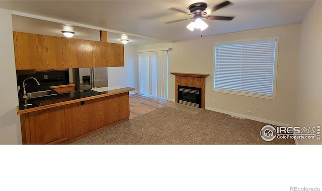 kitchen featuring kitchen peninsula, ceiling fan, stainless steel refrigerator with ice dispenser, a fireplace, and sink