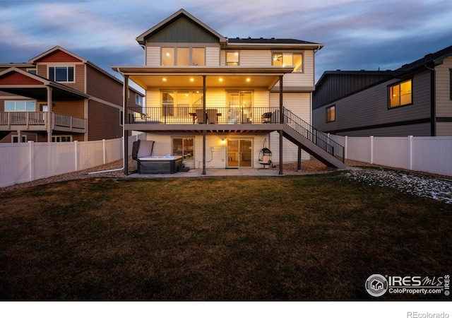 back house at dusk featuring a patio, a lawn, and a hot tub