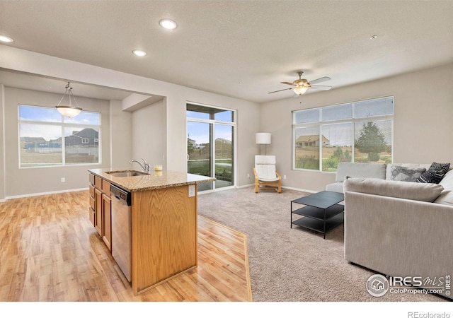 kitchen featuring light stone counters, stainless steel dishwasher, pendant lighting, a kitchen island with sink, and sink