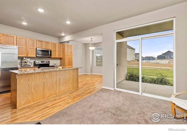 kitchen featuring light brown cabinets, light wood-type flooring, light stone countertops, pendant lighting, and appliances with stainless steel finishes