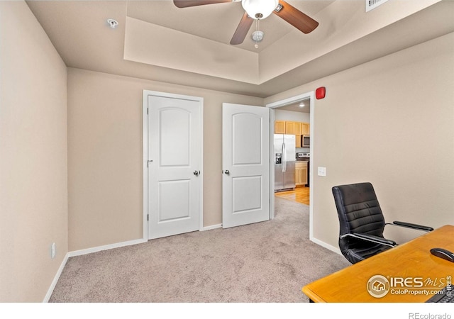 office area with ceiling fan, light carpet, and a raised ceiling