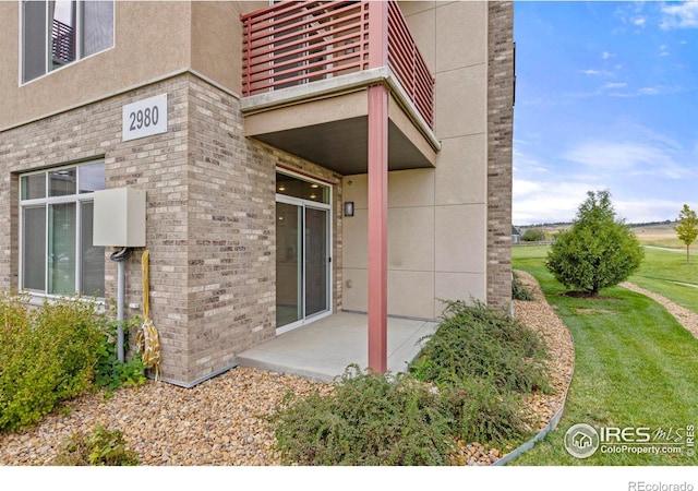 entrance to property featuring a lawn, a balcony, and a patio