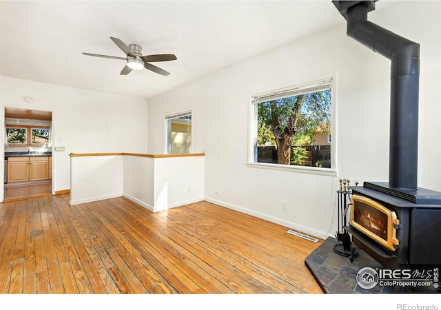 unfurnished living room featuring ceiling fan, light hardwood / wood-style flooring, a wood stove, and sink