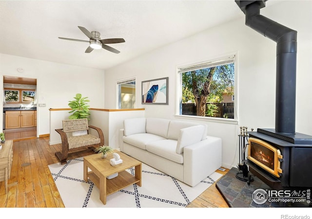 living room featuring light wood-type flooring, ceiling fan, a wood stove, and sink