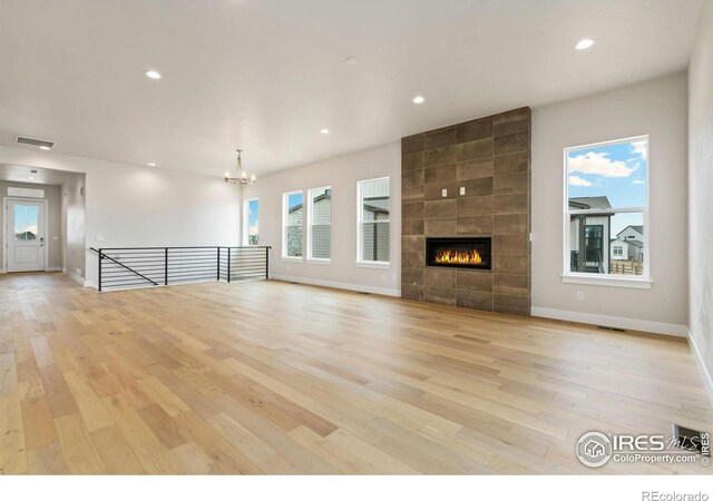 unfurnished living room with visible vents, a notable chandelier, recessed lighting, light wood-style floors, and a tile fireplace