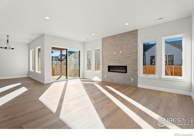 unfurnished living room featuring a tiled fireplace, a notable chandelier, and hardwood / wood-style flooring