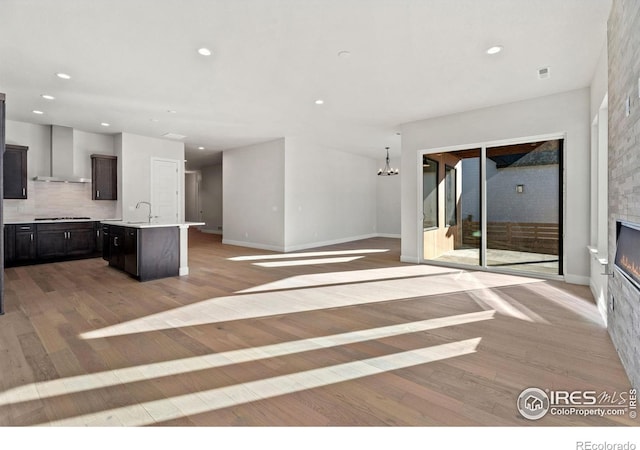 unfurnished living room featuring sink, a notable chandelier, light wood-type flooring, and a fireplace