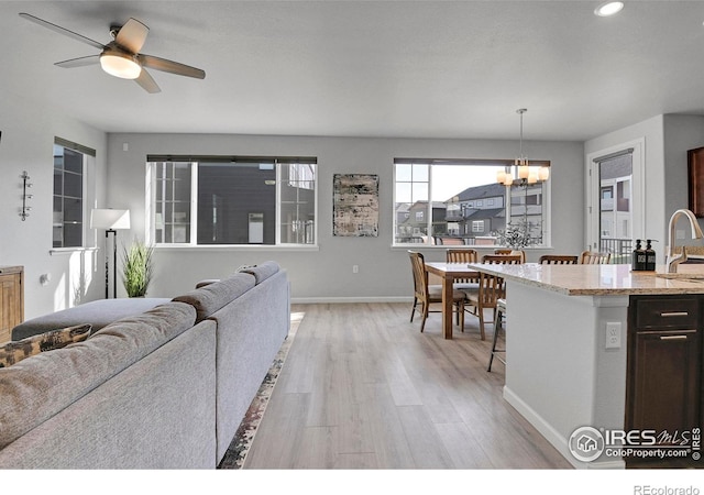 living room with ceiling fan with notable chandelier, light wood-type flooring, and sink