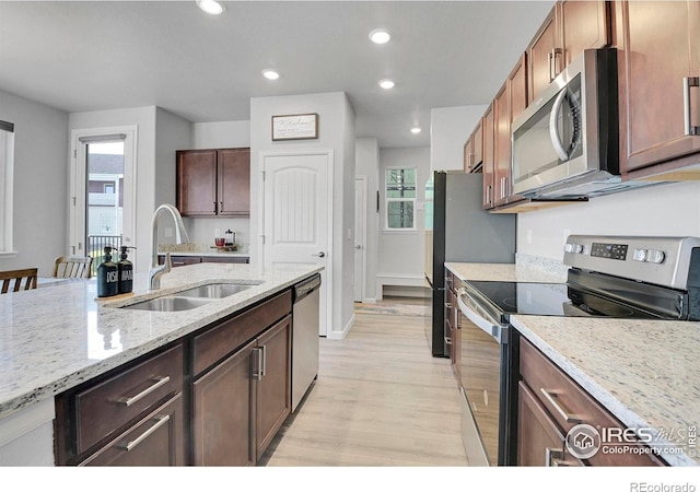 kitchen with appliances with stainless steel finishes, light wood-type flooring, light stone countertops, and sink