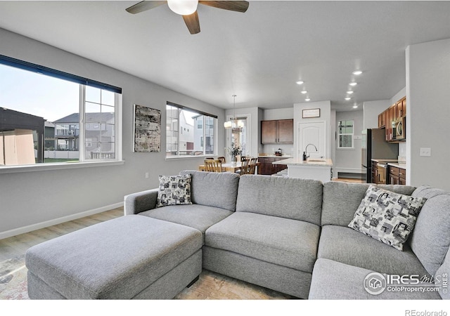 living room featuring sink, ceiling fan with notable chandelier, and light hardwood / wood-style floors