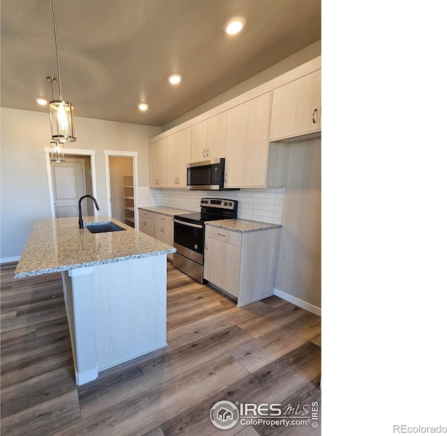 kitchen featuring light stone counters, decorative light fixtures, stainless steel appliances, a kitchen island with sink, and sink