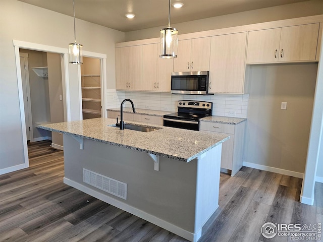 kitchen featuring hanging light fixtures, electric range oven, a kitchen island with sink, and light stone counters