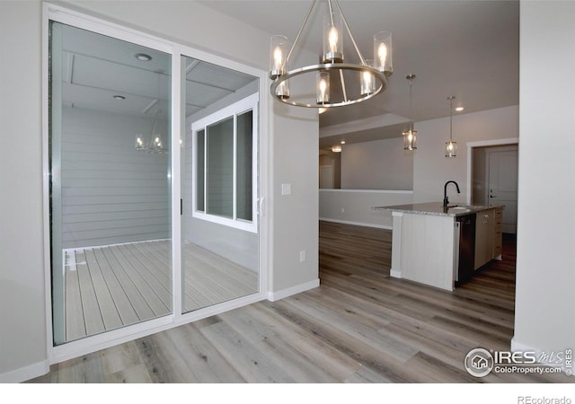 kitchen with a kitchen island with sink, stainless steel dishwasher, sink, decorative light fixtures, and an inviting chandelier