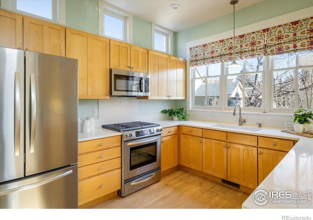 kitchen featuring appliances with stainless steel finishes, light hardwood / wood-style floors, sink, decorative light fixtures, and backsplash