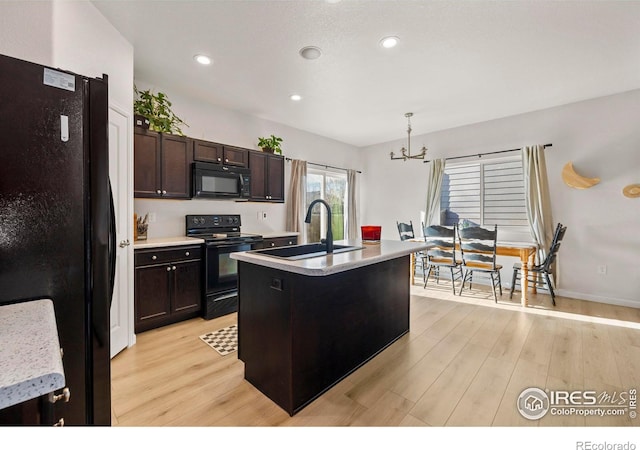 kitchen featuring light hardwood / wood-style flooring, hanging light fixtures, black appliances, a kitchen island with sink, and sink