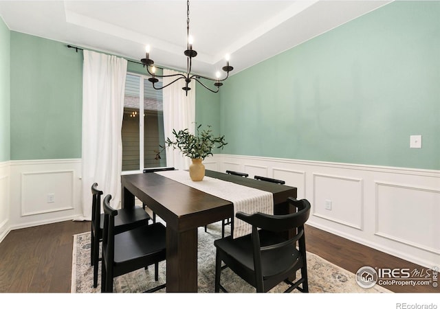 dining space with dark hardwood / wood-style flooring, a notable chandelier, and a raised ceiling