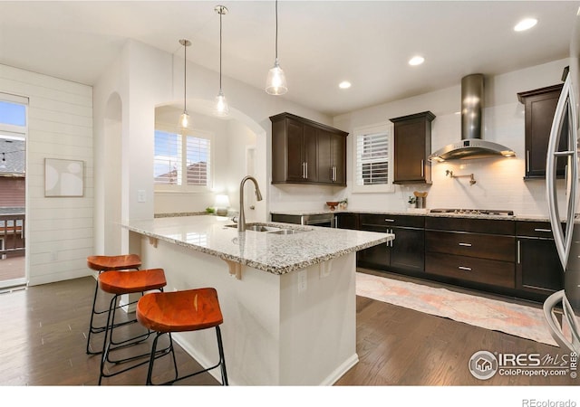 kitchen with sink, light stone counters, wall chimney exhaust hood, a kitchen breakfast bar, and pendant lighting