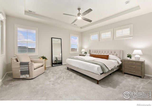 bedroom featuring a raised ceiling, ceiling fan, and light colored carpet