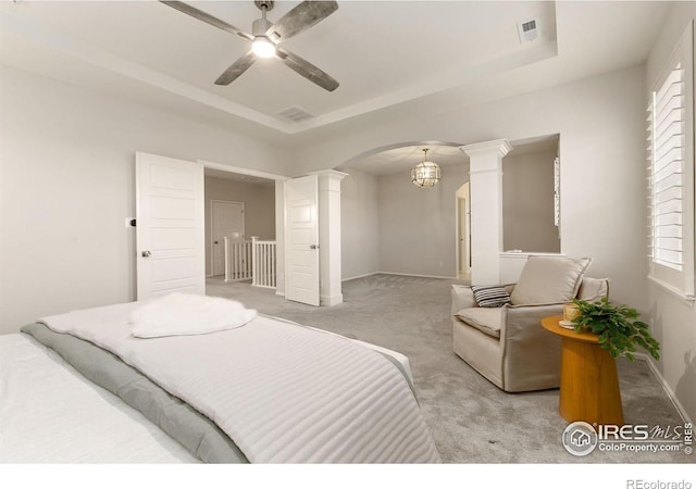 carpeted bedroom featuring ceiling fan with notable chandelier, decorative columns, and a tray ceiling