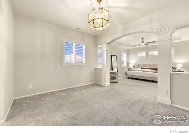 unfurnished bedroom featuring a raised ceiling, an inviting chandelier, carpet floors, and decorative columns