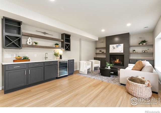 living room featuring indoor bar, a fireplace, light wood-type flooring, and wine cooler