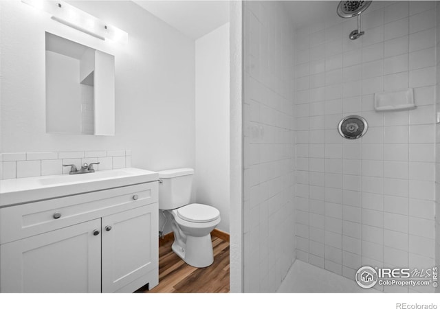 bathroom featuring toilet, vanity, wood-type flooring, and a tile shower