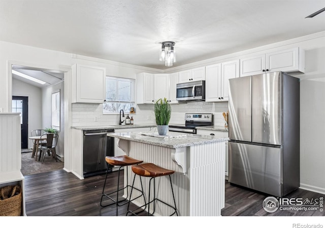 kitchen with stainless steel appliances, a kitchen island, lofted ceiling, white cabinetry, and sink