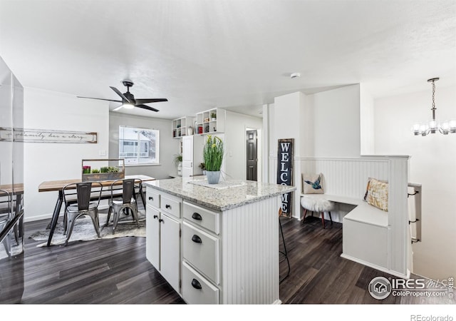 kitchen with dark hardwood / wood-style floors, hanging light fixtures, a center island, ceiling fan with notable chandelier, and white cabinets