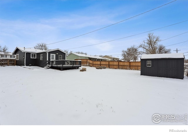 snowy yard featuring a storage shed and a wooden deck