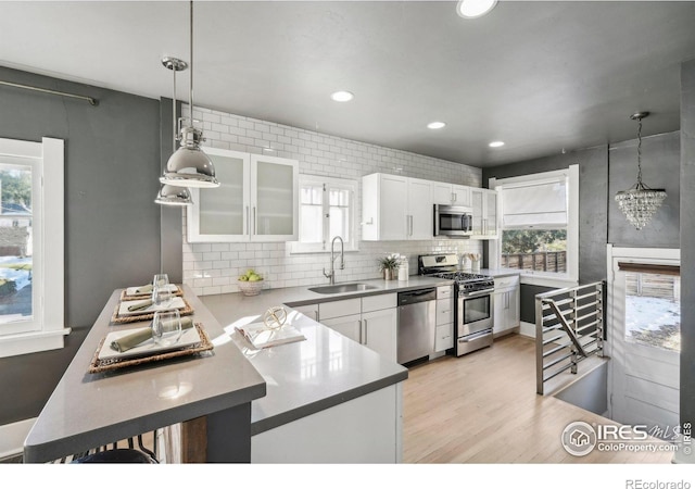 kitchen with decorative light fixtures, stainless steel appliances, light hardwood / wood-style floors, white cabinetry, and sink