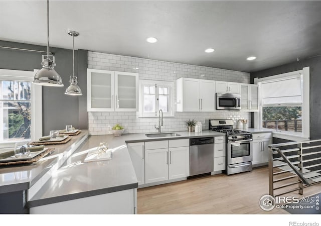 kitchen featuring hanging light fixtures, backsplash, white cabinets, appliances with stainless steel finishes, and sink