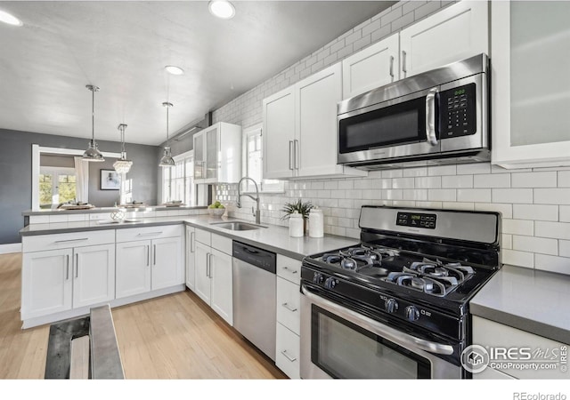 kitchen with kitchen peninsula, decorative light fixtures, stainless steel appliances, white cabinetry, and sink