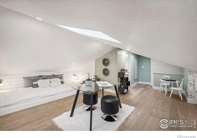 interior space featuring a textured ceiling, lofted ceiling with skylight, and light wood-type flooring