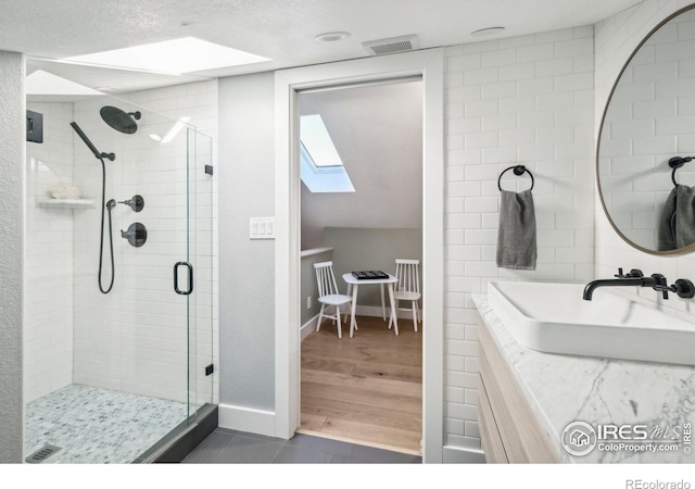 bathroom with a textured ceiling, a skylight, a shower with shower door, and hardwood / wood-style flooring