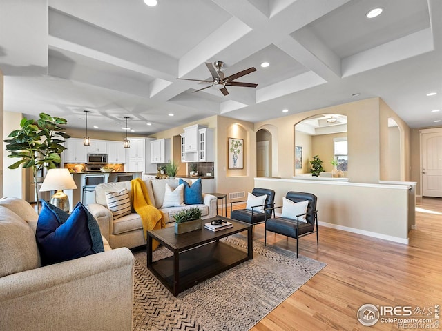 living room featuring coffered ceiling, ceiling fan, beamed ceiling, and light hardwood / wood-style flooring