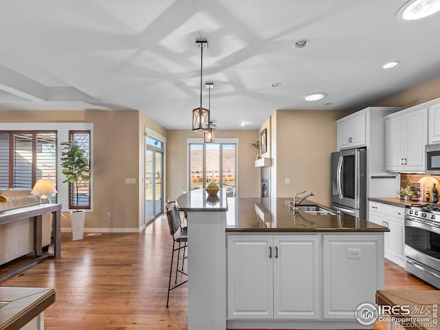 kitchen featuring stainless steel appliances, sink, white cabinetry, hanging light fixtures, and a kitchen island with sink