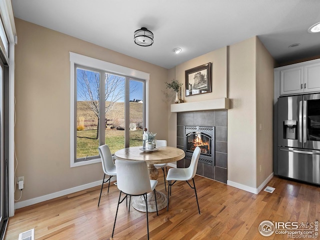 dining room featuring a tiled fireplace and light hardwood / wood-style flooring