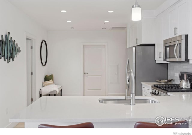 kitchen with stainless steel appliances, a kitchen bar, sink, decorative light fixtures, and backsplash