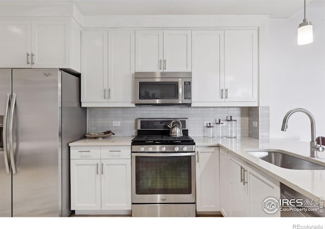 kitchen featuring stainless steel appliances, sink, decorative light fixtures, white cabinetry, and backsplash