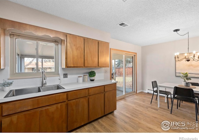 kitchen featuring light wood-type flooring, a notable chandelier, pendant lighting, a textured ceiling, and sink