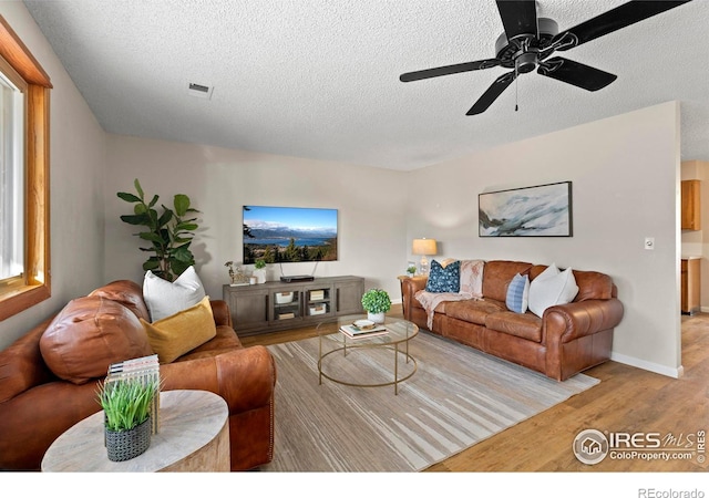 living room with a textured ceiling, ceiling fan, and light hardwood / wood-style flooring