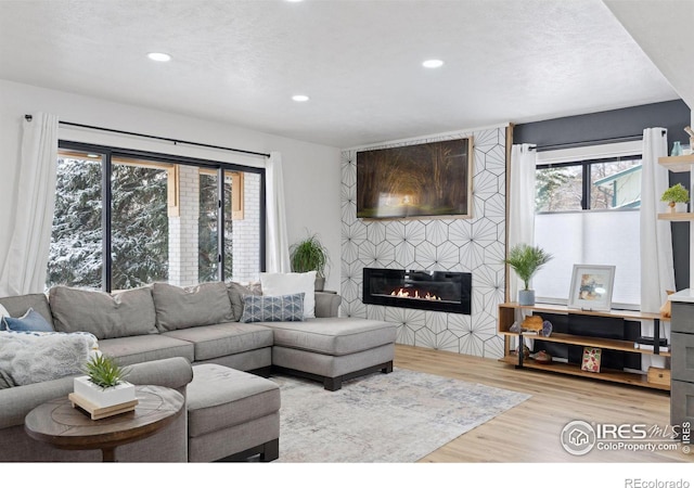 living room with a tiled fireplace, a textured ceiling, and light wood-type flooring