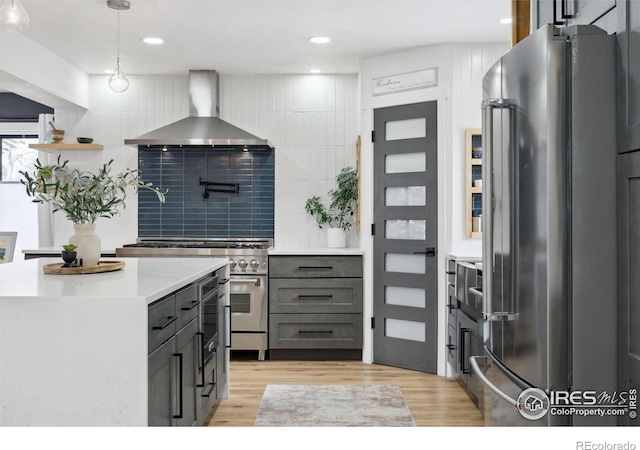 kitchen featuring premium appliances, hanging light fixtures, light wood-type flooring, wall chimney range hood, and backsplash