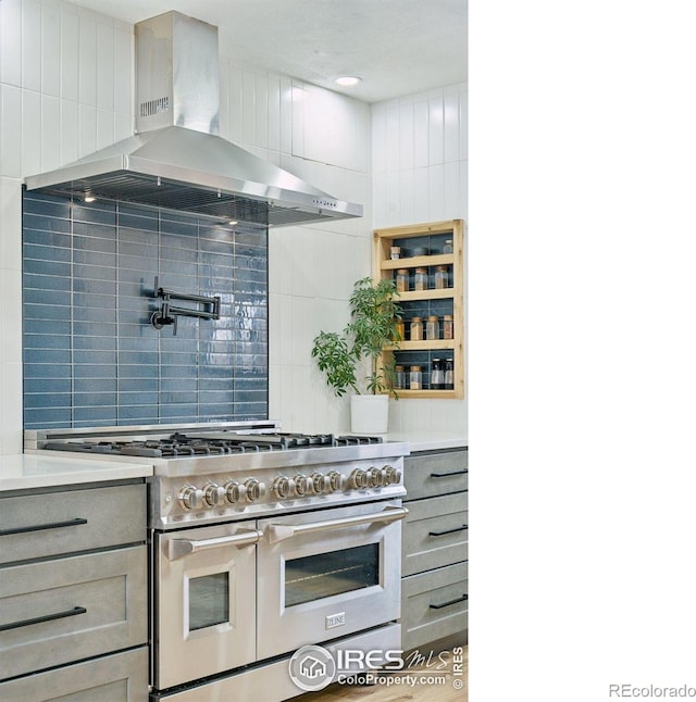 kitchen with range with two ovens, gray cabinetry, light countertops, wall chimney exhaust hood, and tasteful backsplash