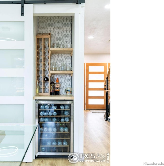 bar featuring wine cooler, a barn door, wood finished floors, and a dry bar