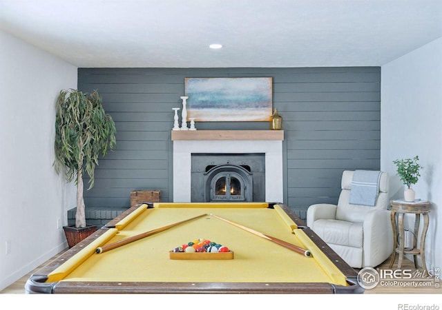 playroom featuring a warm lit fireplace, wooden walls, baseboards, and wood finished floors