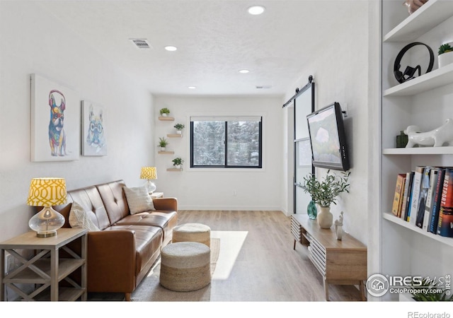 living room with a barn door, built in features, and light wood-type flooring